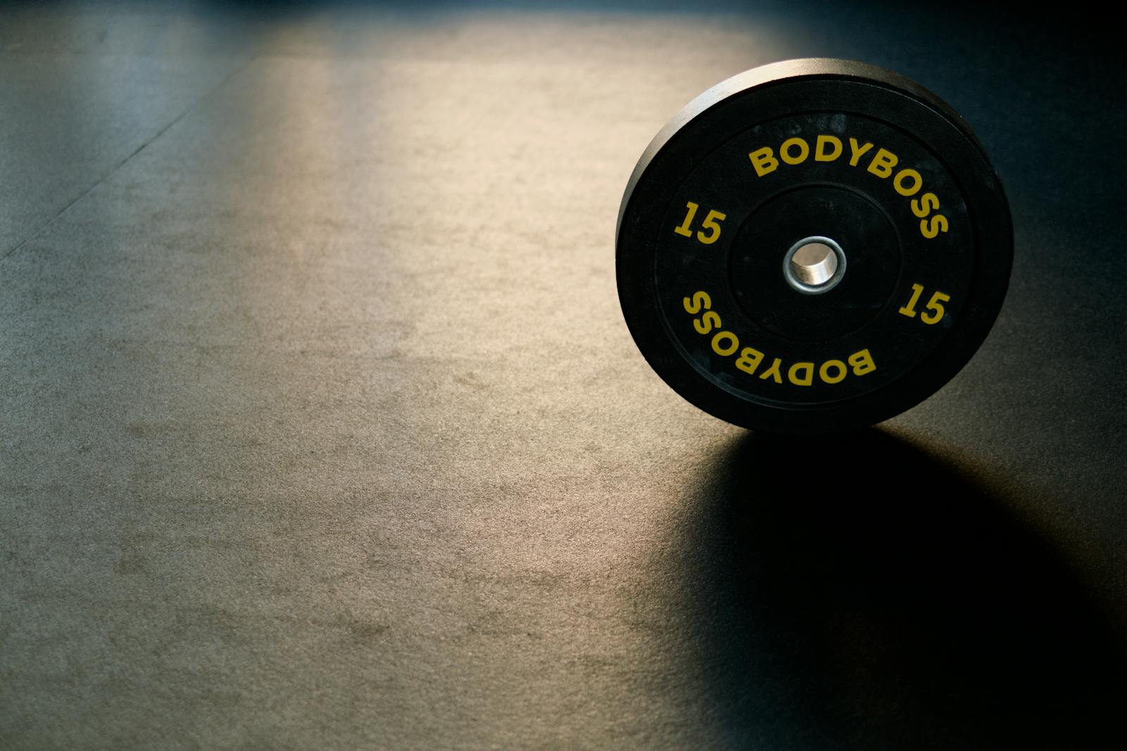 Photo by Ivan Samkov Black BodyBoss weight plate on gym floor, ideal for fitness and workout themes.