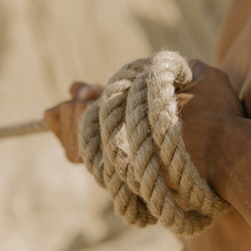 A close-up view of a person's hands tightly gripping a rope during a tug-of-war competition outdoors.