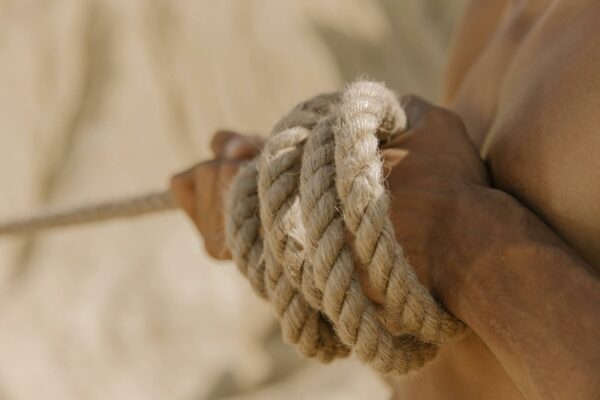 A close-up view of a person's hands tightly gripping a rope during a tug-of-war competition outdoors.